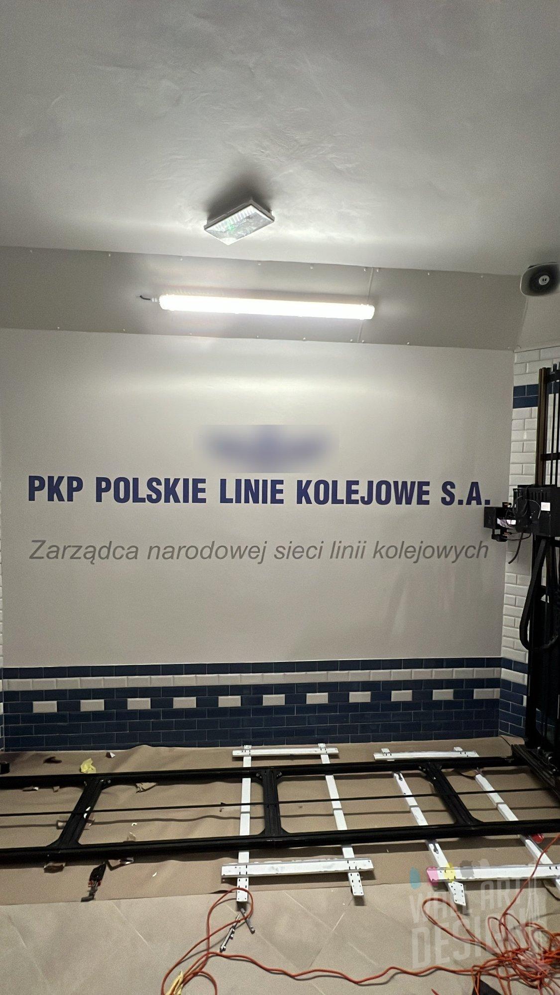 Ściana dworca z wydrukowanym UV napisem PKP Polskie Linie Kolejowe S.A. i drukarką ścienną