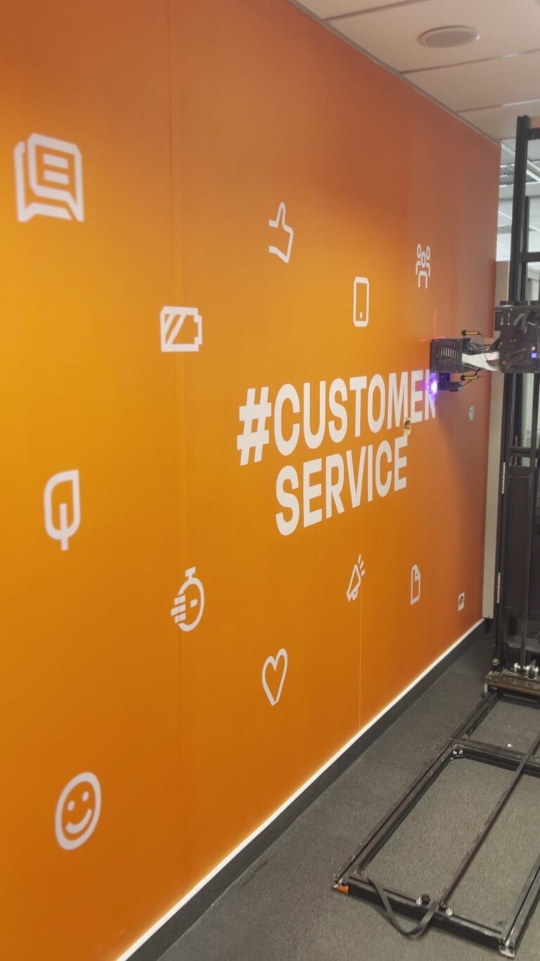 Oznakowanie działu Customer Service w biurze RCI Bank w Warszawie – pomarańczowa ściana z hasztagiem i ikonami wydrukowanymi UV