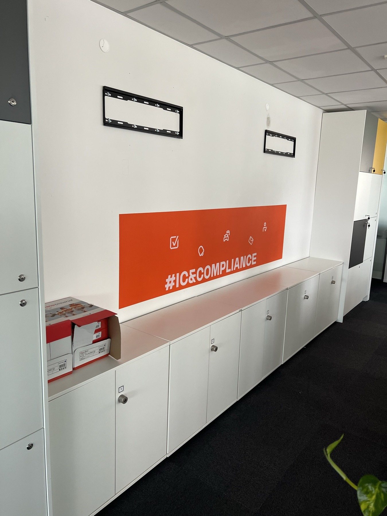 Pomarańczowy pas z napisem #ICECOMPLIANCE nad szafkami w biurze RCI Bank
