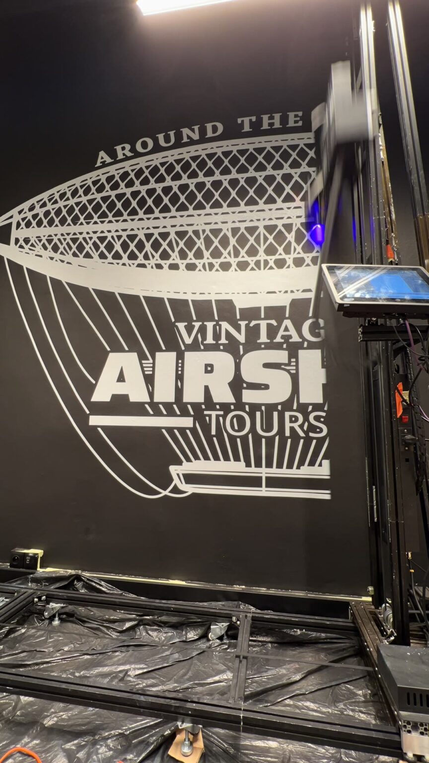 Drukarka ścienna UV drukuje białego sterowca „Vintage Airship Tours” na czarnej ścianie biura Signify