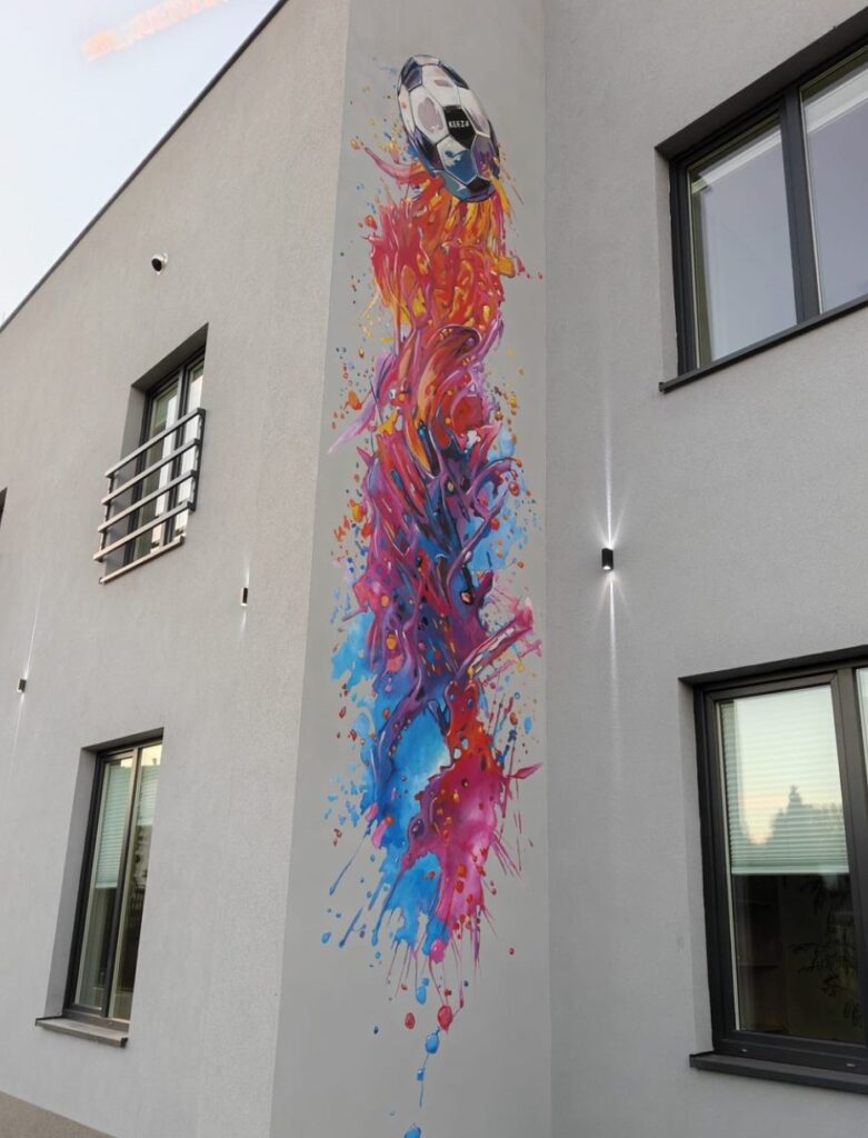 Mural malowany ręcznie – piłka w kolorowych smugach na elewacji budynku